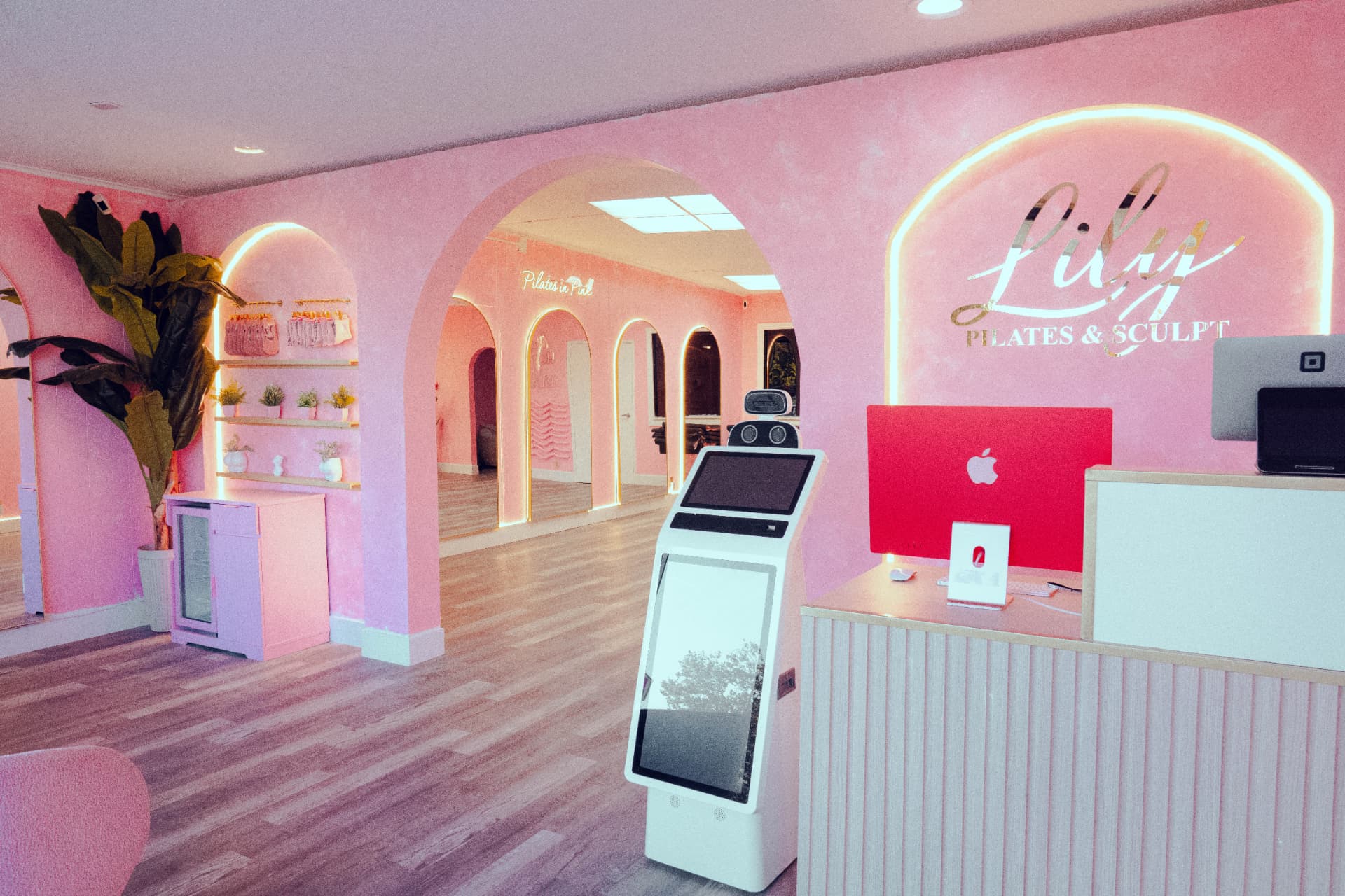 Lily Pilates and Sculpt reception with a fluted front desk, illuminated gold logo sign and pink archways leading into the studio